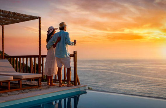 Man and woman on a beach house deck observing the sun setting over the ocean