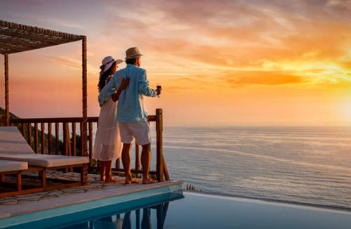 Man and woman on a beach house deck observing the sun setting over the ocean